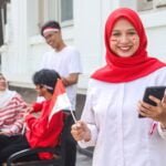 Muslim woman using mobile phone while holding Indonesian flag