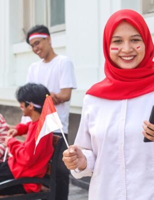 Muslim woman using mobile phone while holding Indonesian flag