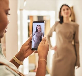 Closeup of woman taking photos of friend trying on clothes in dressing room at boutique